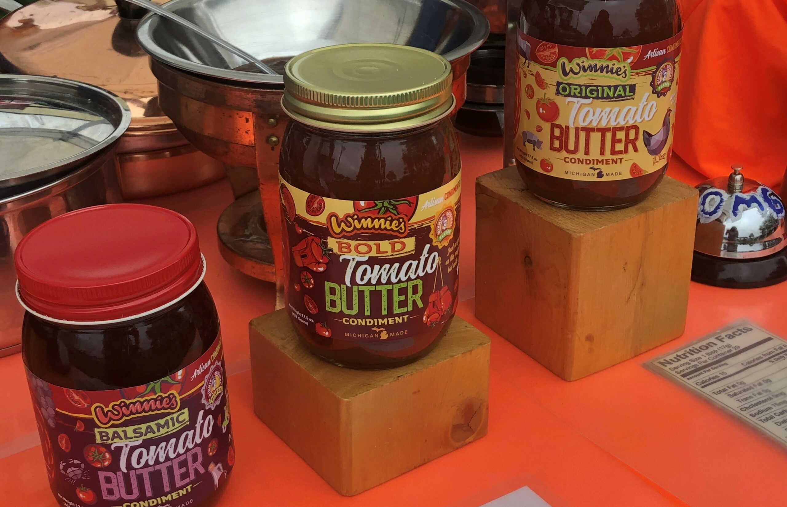 Three jars of Winnie's bold tomato butter sitting on a table with orange table cloth.